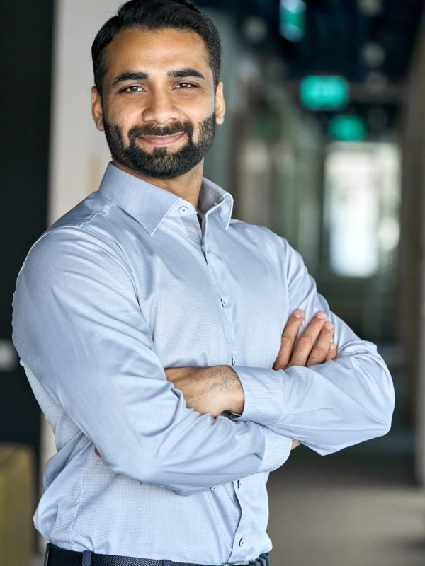 Smiling happy successful ceo financial manager confident bearded indian businessman looking at camera standing with arms crossed. Handsome classy corporation owner. Vertical business portrait.
